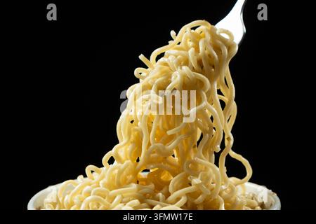 Cooked instant ramen noodles lifted on fork against black background. Stock Photo