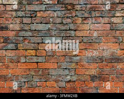 Front-on view of a weathered old red brick wall showing varied colours, worn mortar and irregular historic brickwork. Stock Photo