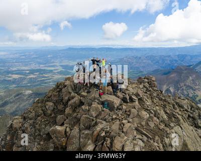 Aerial view of a group of hikers standing on the rocky summit of Mount Sneffels in the San Juan Mountains, surrounded by a vast mountain landscape in Stock Photo