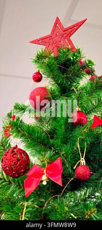 Red glitter star topper and red baubles decorate a Christmas tree with bow, bell and pine cone details in Granada, Spain. Stock Photo