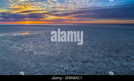 Aerial view of a frozen sea covered with ice floes under a vibrant sunset sky in Latvia. Stock Photo