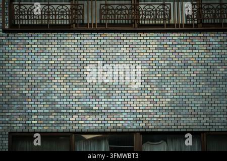 The image shows a close-up of an opalescent ceramic tile facade featuring a mosaic of small rectangular tiles in various shades of blue, green, pink, Stock Photo