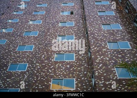 The exterior wall of a modern building is covered in a mosaic pattern of small red, dark brown, and tan bricks, with numerous uniformly spaced rectang Stock Photo