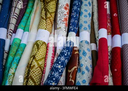 Multiple rolls of traditional Japanese kimono fabrics are neatly stacked, bound with white paper bands, showcasing a variety of colors including blue, Stock Photo
