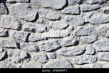 Wall made of natural stone with mortar joints, featuring rough and irregular stones in light gray and white shades. Close up, background and texture. Stock Photo