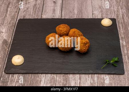 Five crispy falafel balls stacked in a cluster with two creamy sauce dollops and a parsley sprig on black slate over gray wood Stock Photo