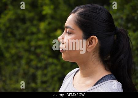 Midadult female standing facing-left in park, gray athletic top, bra-strap, stud earring Stock Photo