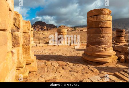View of ancient stone columns and ruins of the Great Temple in the desert landscape of Petra with rocky mountains under a cloudy sky in Wadi Musa, Ma' Stock Photo