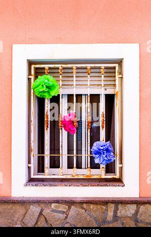 Three brightly colored tissue paper pom poms in shades of green pink and blue are securely attached to a rusty white metal security bar grid covering Stock Photo