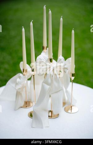 Elegant white taper candles in gold holders decorated with white silk bows Stock Photo