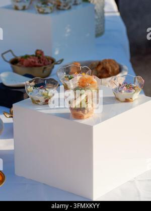 Plastic cups with layered shrimp and vegetable appetizers served on a white table at an outdoor event. Stock Photo