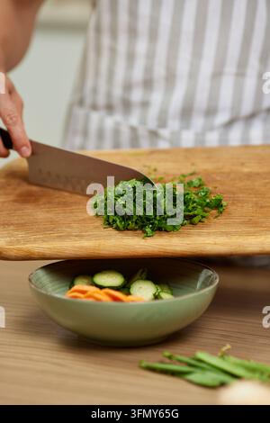Person chopping fresh parsley on cutting board for healthy meal Stock Photo