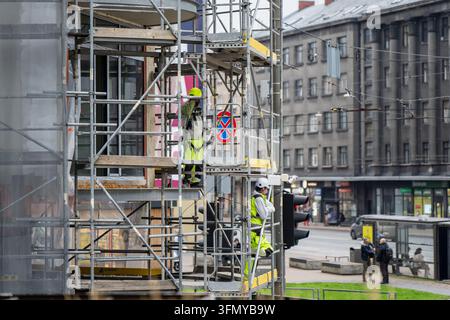 Construction workers in high visibility clothing stand on scaffold levels near a traffic signal, representing facade access and urban site coordinatio Stock Photo