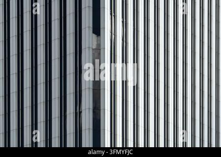 Close-up of a modern office building facade featuring reflective windows, vertical metal panels, and repeating geometric lines, creating an abstract c Stock Photo