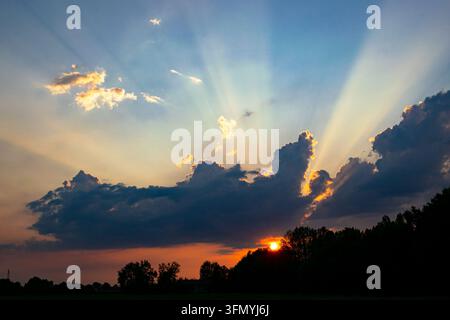 Sunrays or crepuscular rays from behind the clouds during a colorful sunset. Stock Photo