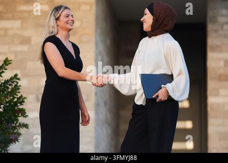Businesswomen Shaking Hands Outside Office Building, Diverse Professionals Meeting With Laptop Stock Photo
