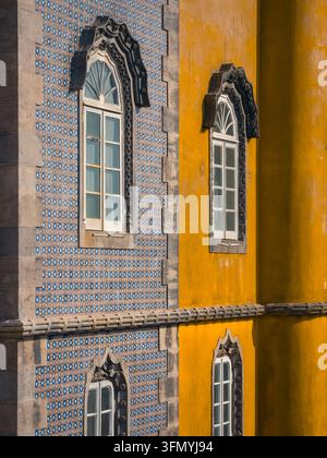 Decorative arched windows and colorful azulejo tilework on the vivid yellow facade of Pena Palace in Sintra, Portugal, captured in summer sunlight nea Stock Photo