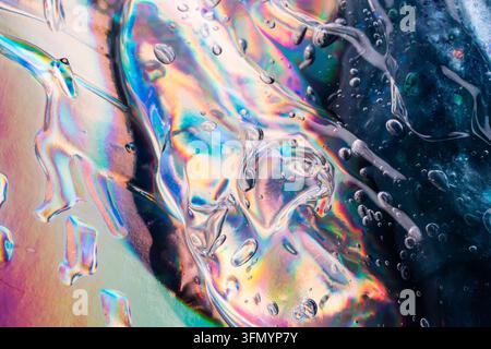 Close-up abstract texture of clear water droplets on an iridescent surface, creating colorful rainbow refraction, fluid reflections, and dark blue con Stock Photo