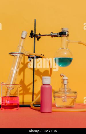 Pink cosmetic shampoo bottle stands beside laboratory glassware, colorful liquids, and scientific apparatus on a vivid yellow background, illustrating Stock Photo