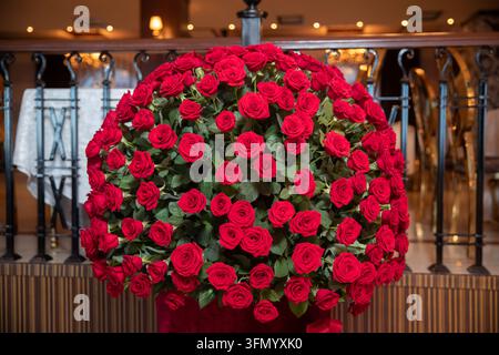 A stunning floral centerpiece decorating an elegant restaurant interior for a event. Huge arrangement of luxury red roses assembled in a large round Stock Photo