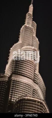 A dramatic nighttime photograph showcases the towering Burj Khalifa in Dubai, illuminated against the dark sky. The building’s intricate design is hig Stock Photo