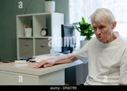 Elderly man sitting calmly at desk in doctor office waiting for medical consultation. Senior patient attending health checkup appointment and wellness evaluation in clinic examination room setting Stock Photo