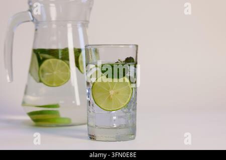 Infused water with lime, mint, and ice cubes in a glass and pitcher Stock Photo