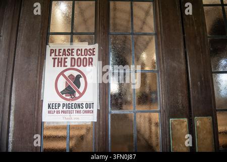 Printed notice requesting visitors close the door to keep pigeons out on the wooden entrance door of St Mary's Church, Tenby, Wales. Stock Photo