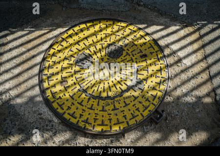 A yellow circular manhole cover with a raised pattern of small 'T' shapes and a large smiley face design, centered with the letters 'TIC' and marked ' Stock Photo