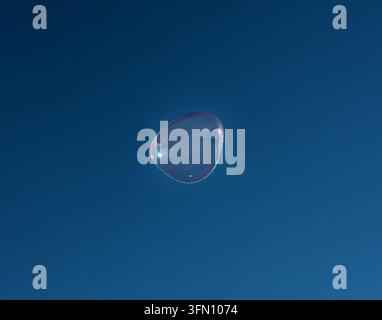 Iridescent Giant Soap Bubble Floating High Against a Deep Blue Sky Stock Photo