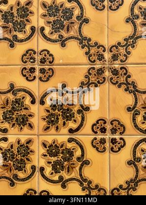 Ochre Portuguese azulejo wall tiles with a raised dark green floral and scroll pattern in Portugal Stock Photo