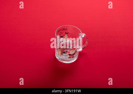 Clear glass mug decorated with festive Christmas characters including Santa Claus, snowman, and reindeer. Text reads Feliz Natal. Studio shot against Stock Photo