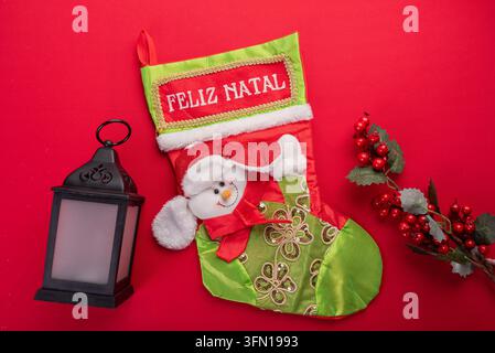 Flat lay arrangement featuring festive Christmas stocking with snowman design and Feliz Natal text, alongside a decorative lantern and berry branch ag Stock Photo