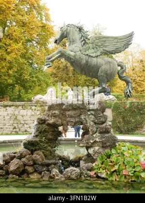 Dynamic bronze statue of the winged horse Pegasus rearing above the stone grotto fountain, framed by vivid golden autumn trees in Mirabell Palace Gard Stock Photo