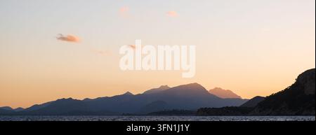 Golden sunset over Mallorca's mountain silhouettes reflected on a tranquil Mediterranean sea, ideal for travel and nature concepts. Stock Photo