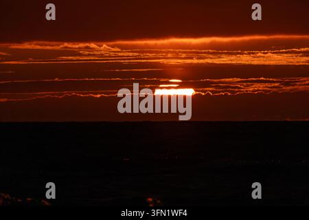 Sun glowing behind dark sunset cloud layers close up Stock Photo