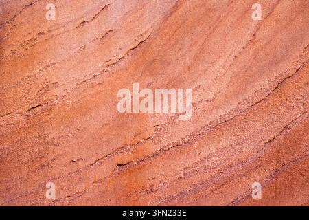 Close-up of orange sandstone surface with fine wavy sedimentary layers, natural cracks and subtle variations in reddish and pink tones Stock Photo