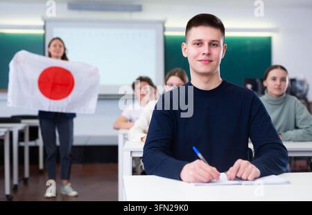 High school teacher tells students about Japan and holds a Japanese flag in hands. Stock Photo