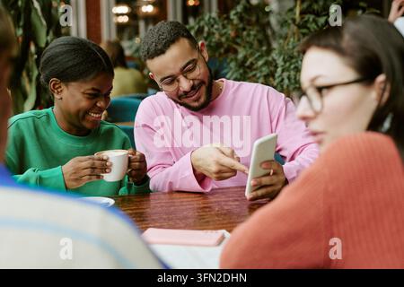 Diverse Friends Using Smartphone and Drinking Coffee in Cafe Stock Photo
