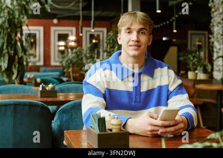 Portrait of Man Holding Smartphone Sitting at Table in Cafe Stock Photo