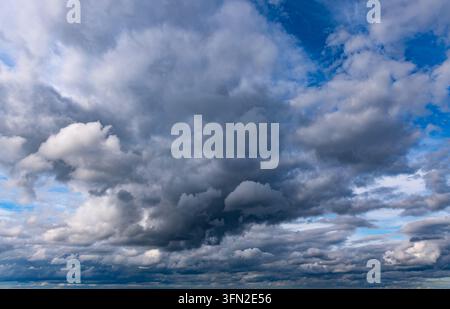 Powerful dark storm clouds mixed with bright cumulus formations and patches of blue sky create a dramatic and atmospheric natural cloudscape. Stock Photo