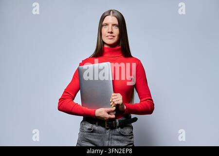 Confident woman in red turtleneck holding closed laptop studio shot Stock Photo