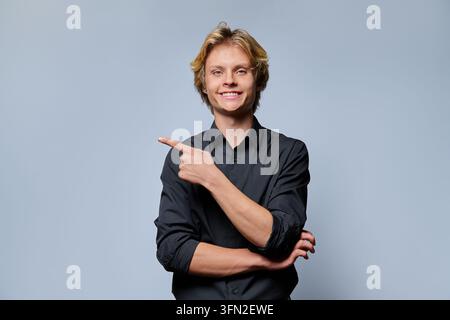Smiling young man pointing index finger to side copy space against grey background Stock Photo