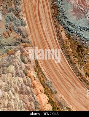 Aerial view of a large-scale mining operation featuring a wide haul road with visible tire tracks, excavated earth, and piles of mine tailings in Thab Stock Photo