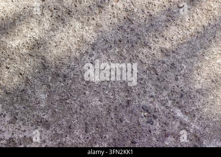 Detailed close-up view of a rough concrete floor texture with speckled stone aggregate, dark cement grain, and natural sunlight shadows. High Quality Photo Stock Photo