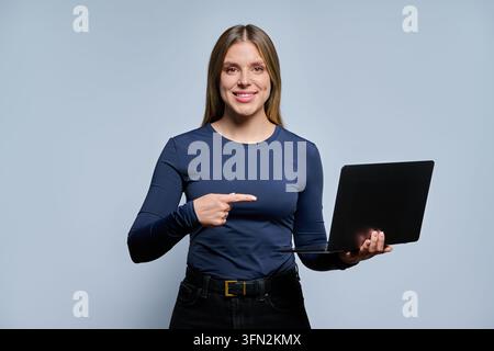 Smiling young woman holding laptop and pointing at it Stock Photo