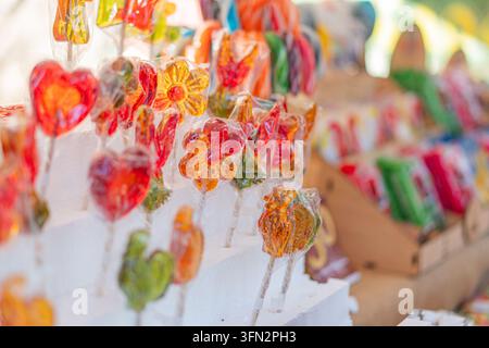 A collection of colorful, handcrafted decorative lollipops in various shapes flowers, hearts, abstract displayed on white stands Vibrant hues red, ora Stock Photo