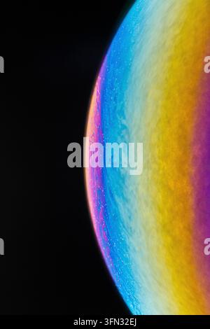 Macro close-up of a colorful iridescent soap bubble curve resembling a planet horizon against a black background. Stock Photo