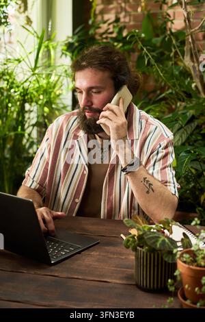 Bearded Man Talking on Smartphone and Working on Laptop Stock Photo