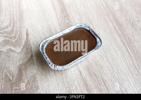 Smooth chocolate dessert or chocolate pudding served in a small rectangular aluminum foil tray on a light wooden table with generous copy space around Stock Photo